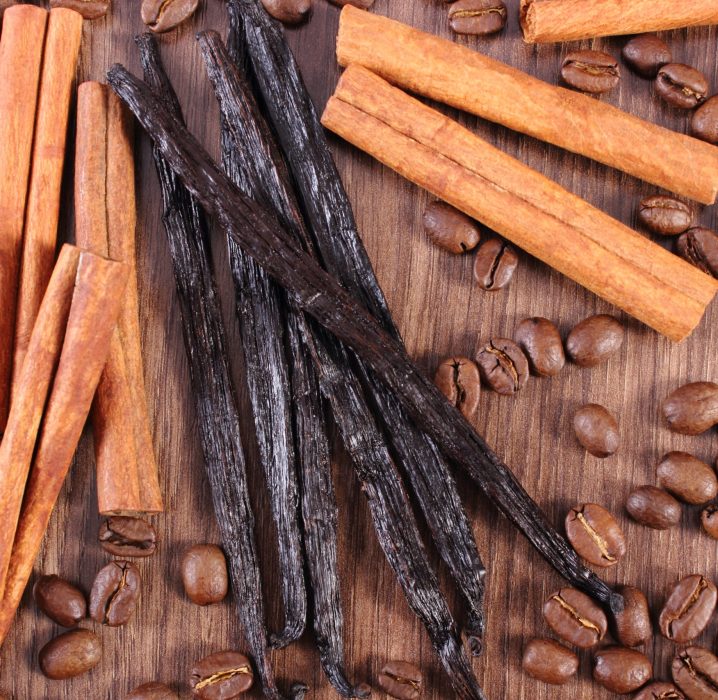 Fresh fragrant vanilla pods, cinnamon sticks and coffee grains on wooden plank, seasoning ingredients for cooking or baking